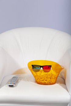 3D glasses, popcorn and a remote control on a sofa.