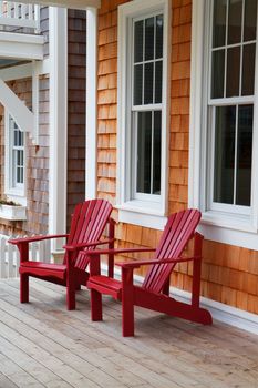 Two red Adirondack chairs on a wood deck against a brown wood shake home