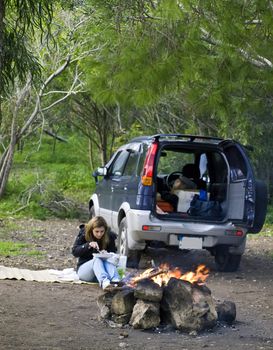 A woman next to a SUV and burning bonfire excellent to portray outdoor leisure activities such as camping