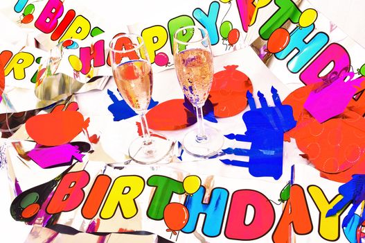 shiny colorful streamer of birthday greeting with cutouts of cake candles and balloons  with two glasses of pink bubbly champagne
