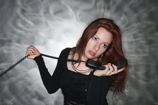 Portrait of pretty young redhead woman holding telephone receiver to ear.