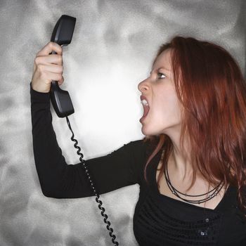 Portrait of pretty young redhead woman holding telephone receiver and yelling.