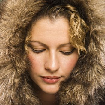 Caucasian young adult woman wearing fur hood with eyes closed.