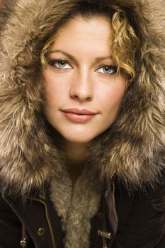 Caucasian young adult woman wearing coat with fur hood looking at viewer.