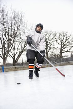 Boy in ice hockey uniform skating on ice rink moving puck.