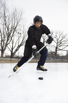 Boy in ice hockey uniform skating on ice rink moving puck.