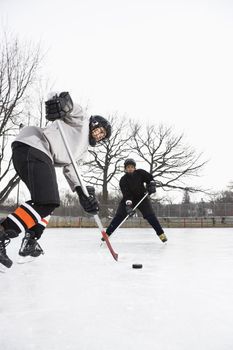 Two boys in ice hockey uniforms skating on ice rink moving puck.