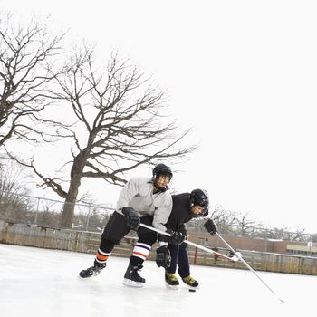 Two boys in ice hockey uniforms playing hockey on ice rink.