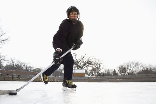 Boy in ice hockey uniform skating on ice rink moving puck.