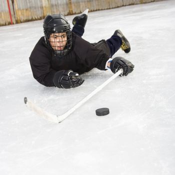 Ice hockey player boy in uniform sliding on ice holding stick out towards puck.