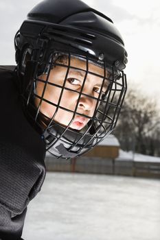 Ice hockey player boy in uniform and cage helmet making mean face.