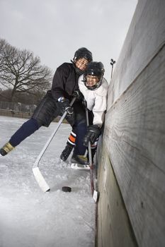 Ice hockey player boy slamming other player into wall trying to get to puck.