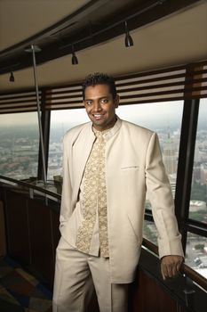 Portrait of young adult male Indian standing near window in tower restaurant smiling at viewer.