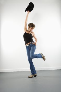 Full length portrait of pretty Caucasian woman holding up cowboy hat in playful pose.