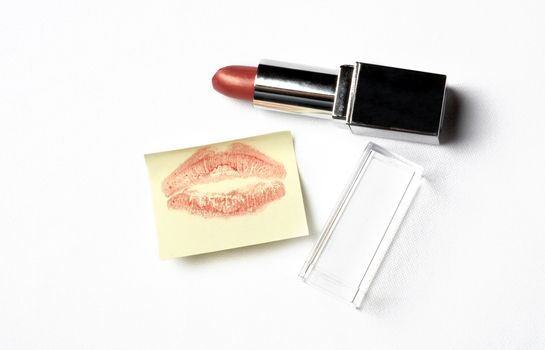 red lipstick and yellow sticker note with kiss over white