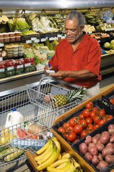 Middle aged African American man in grocery store writing on shopping list.