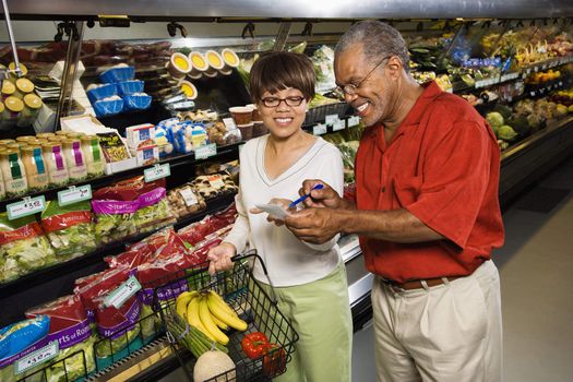 Middle aged African American man and woman in grocery store smiling and pointing at shopping list.