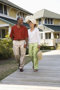 African American middle aged couple holding hands strolling on wooden walkway.