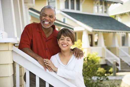 African American middle aged couple standing together on stairs outside home.