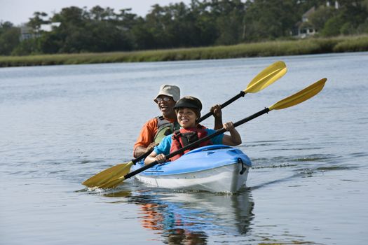African American middle-aged couple smiling and paddling kayak.