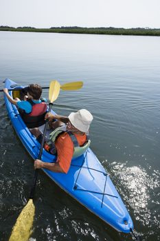 Back view of African American middle-aged couple paddling kayak.