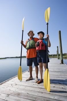 African American middle-aged couple standing on boat dock holding paddles and smiling at viewer.