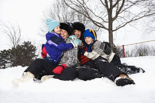 Portrait of happy Caucasian family of four sitting in snow smiling at veiwer.