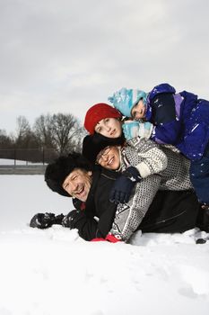 Portrait of happy Caucasian family of four lying stacked on top of each other in snow smiling at viewer.