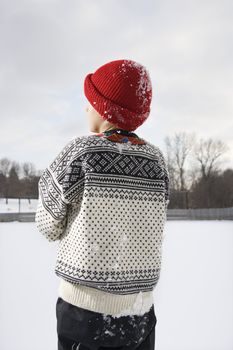 Back view of Caucasian boy wearing sweater and red winter cap.