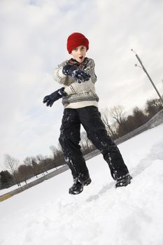 Caucasian boy with mouth open wearing sweater and red winter cap gesturing with arms and hands.