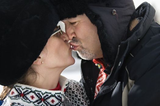 Side view of Caucasian middle aged man and woman in winter clothing kissing.