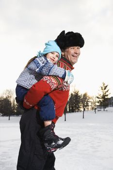 Caucasian middle aged man holding Caucasian litte girl piggyback style smiling and looking at viewer smiling.