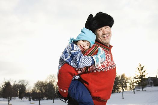 Portrait of Caucasian middle aged man holding Caucasian litte girl piggyback style smiling and looking at viewer.