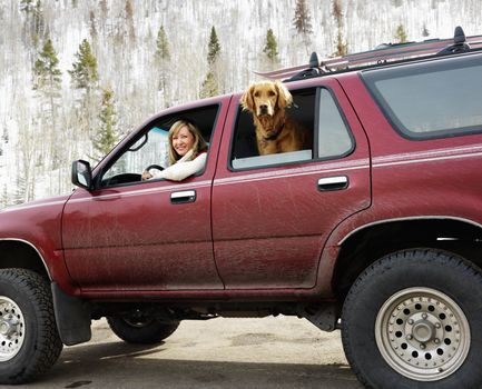 Woman and dog in dirt splattered SUV looking out windows in snowy countryside.