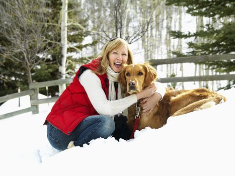 Woman hugging dog and smiling in snow covered Colorado landscape.