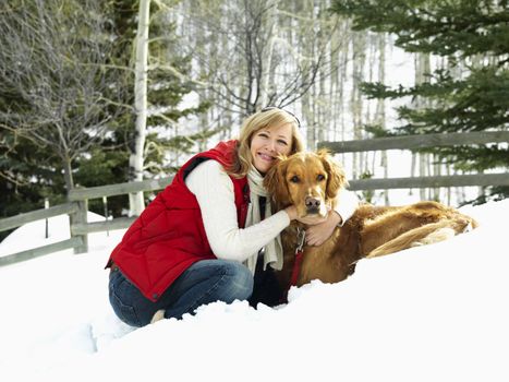 Woman hugging dog and smiling in snow covered Colorado landscape.