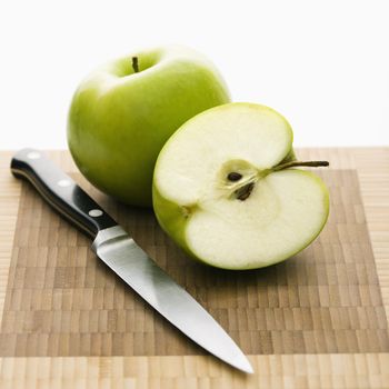 Still life of green apples and knife on cutting board.