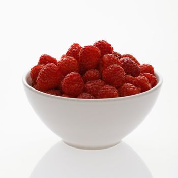 Bowl of raspberries against white background.