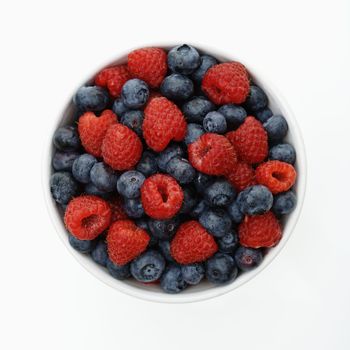 Bowl of mixed blueberries and raspberries on white background.