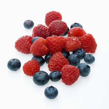 Mixed blueberries and raspberries on white background.