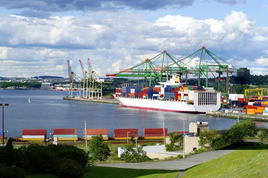 cargo ship at the waterfront with crane, storage, crates, railroad track and cargo train in foreground