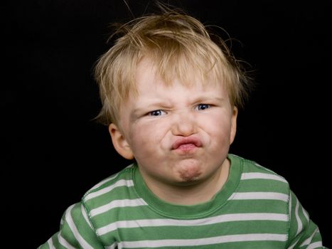 Little boy making funny face on black background. Boy have blue eyes and blond hair and have a bit of dirt on his face