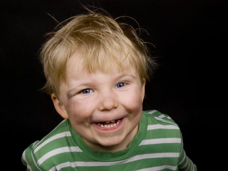 Smiling little boy on black background. Boy have blue eyes, blond hair and a bit of dirt on his face
