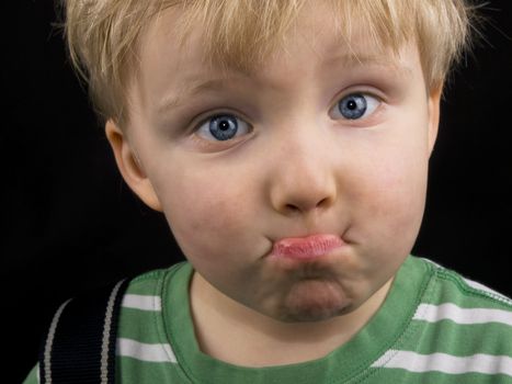 Little boy making funny face on black background. Boy have blue eyes and blond hair and have a bit of dirt on his face