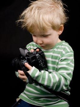 Smiling little boy with digital camera on black background. Boy have blue eyes and blond hair