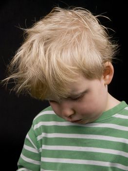 Very sad litlle boy on black background. Boy have blond hair and a bit of dirt on face