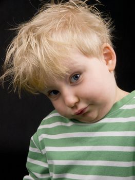 Little boy making funny face on black background. Boy have blue eyes and blond hair and have a bit of dirt on his face