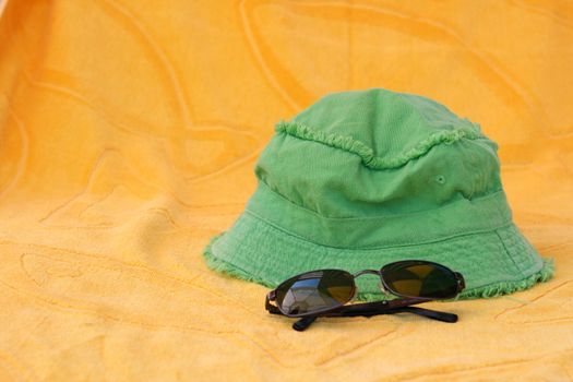 summer accessories green hat and black sunclasses on yellow towel