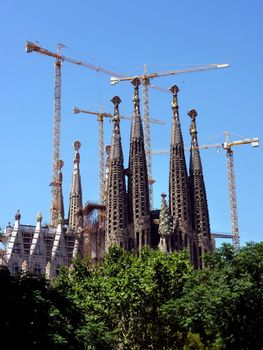View of the back of the Sagrada familia church in Barcelona, Spain, with its towers and the cranes arround, by beautiful weather
