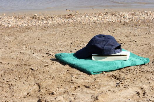 blue baseball hat on green towel by the see and book